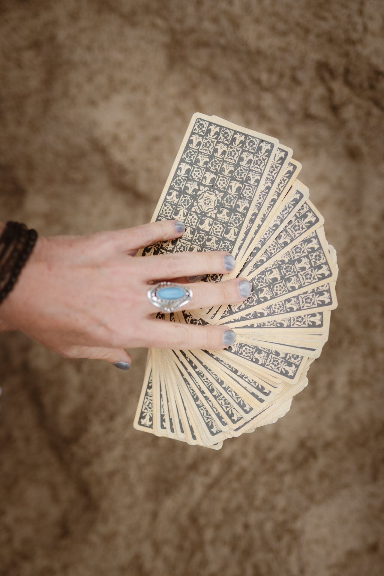 A hand fanning a deck of tarot cards over warm sand
