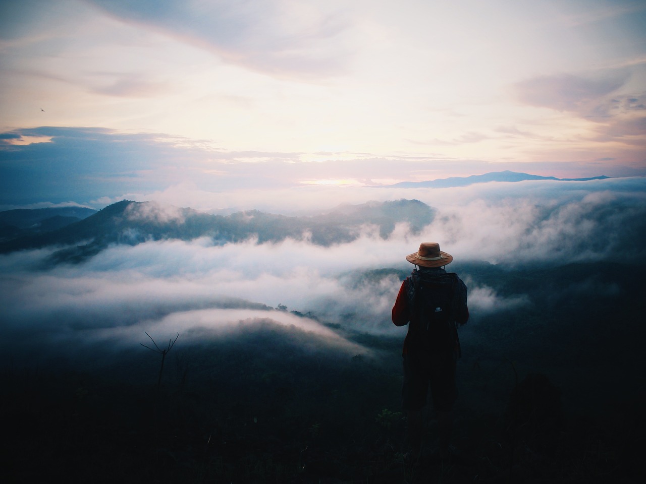 Solitary figure gazing across a sea of clouds at dawn