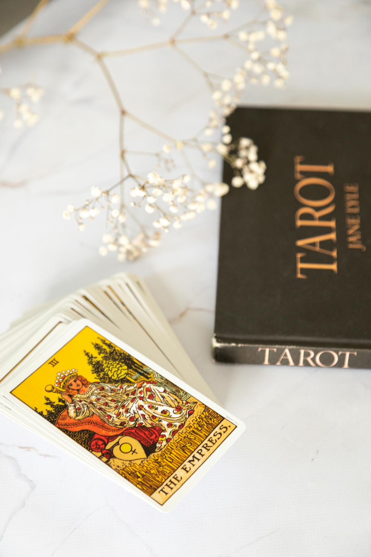 The Empress card resting beside a tarot guidebook and dried flowers