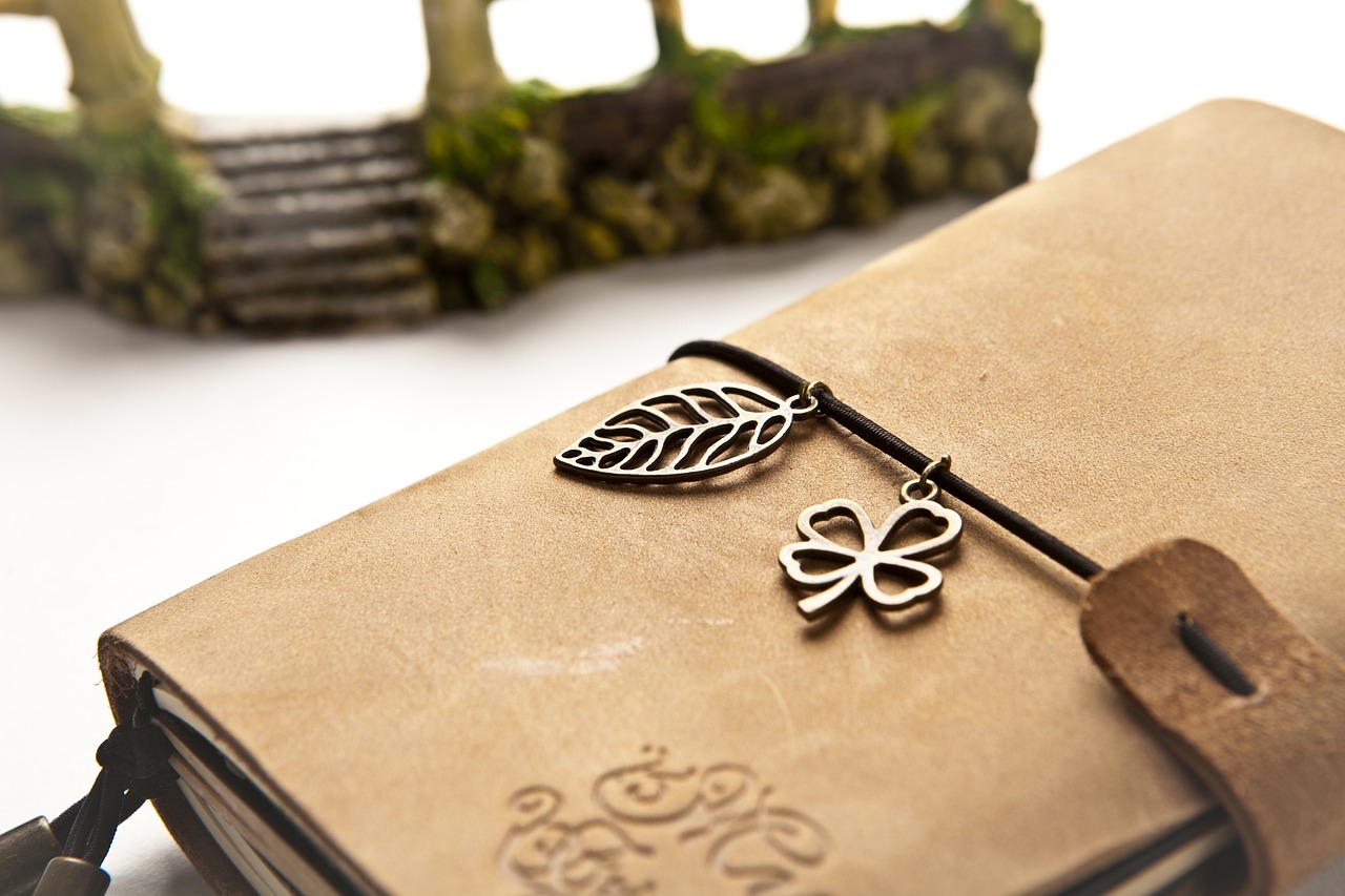 Leather journal with leaf and clover charms beside a stone arch